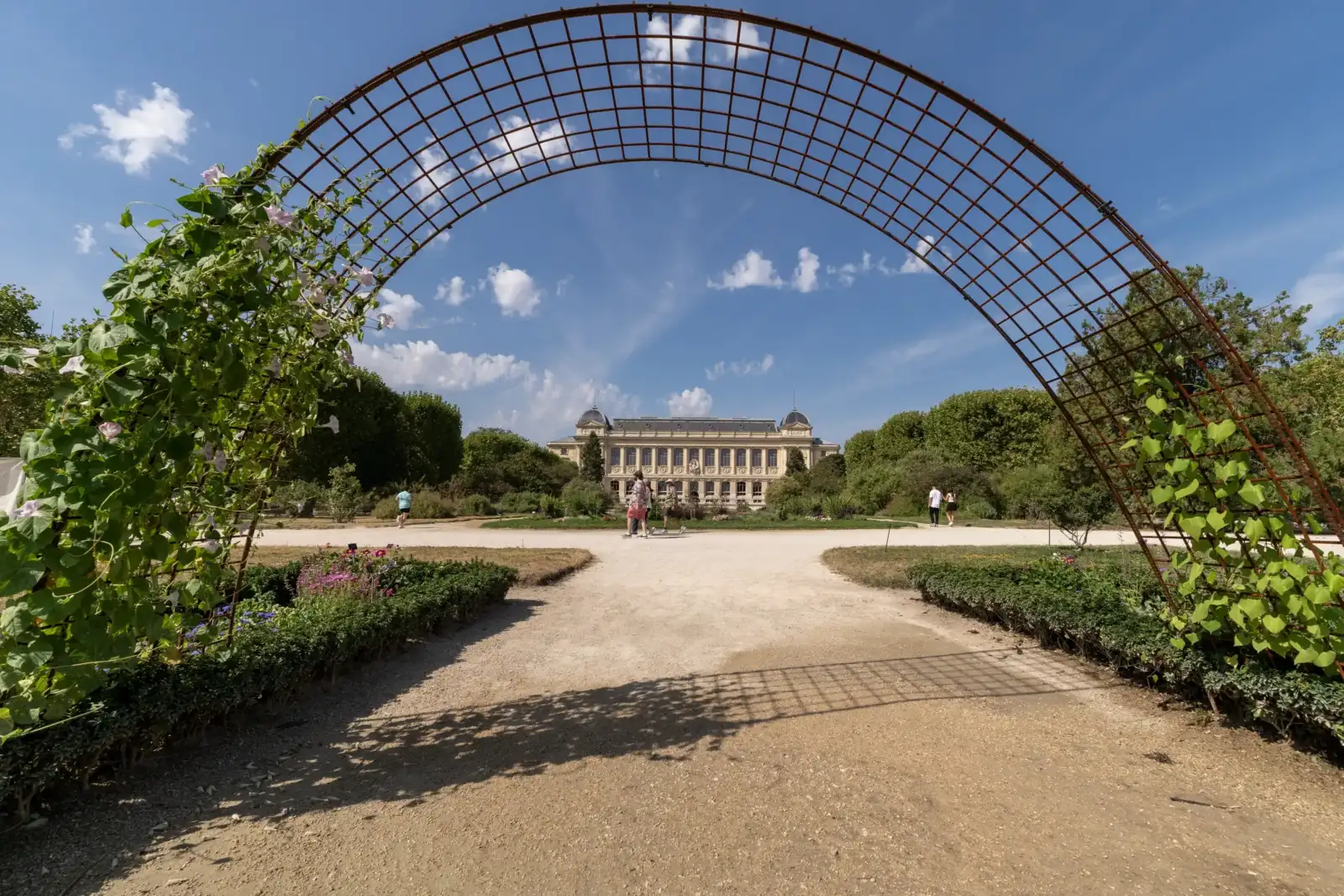 Une grande arche métallique fleurie encadre la superbe façade du Jardin des Plantes à Paris.