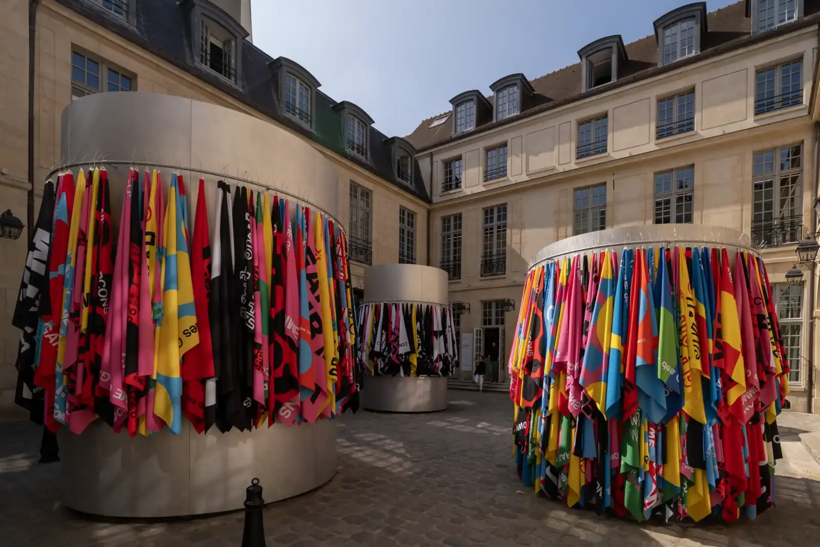 Trois structures cylindriques ornées de drapeaux colorés dressées au centre d une cour pavée parisienne