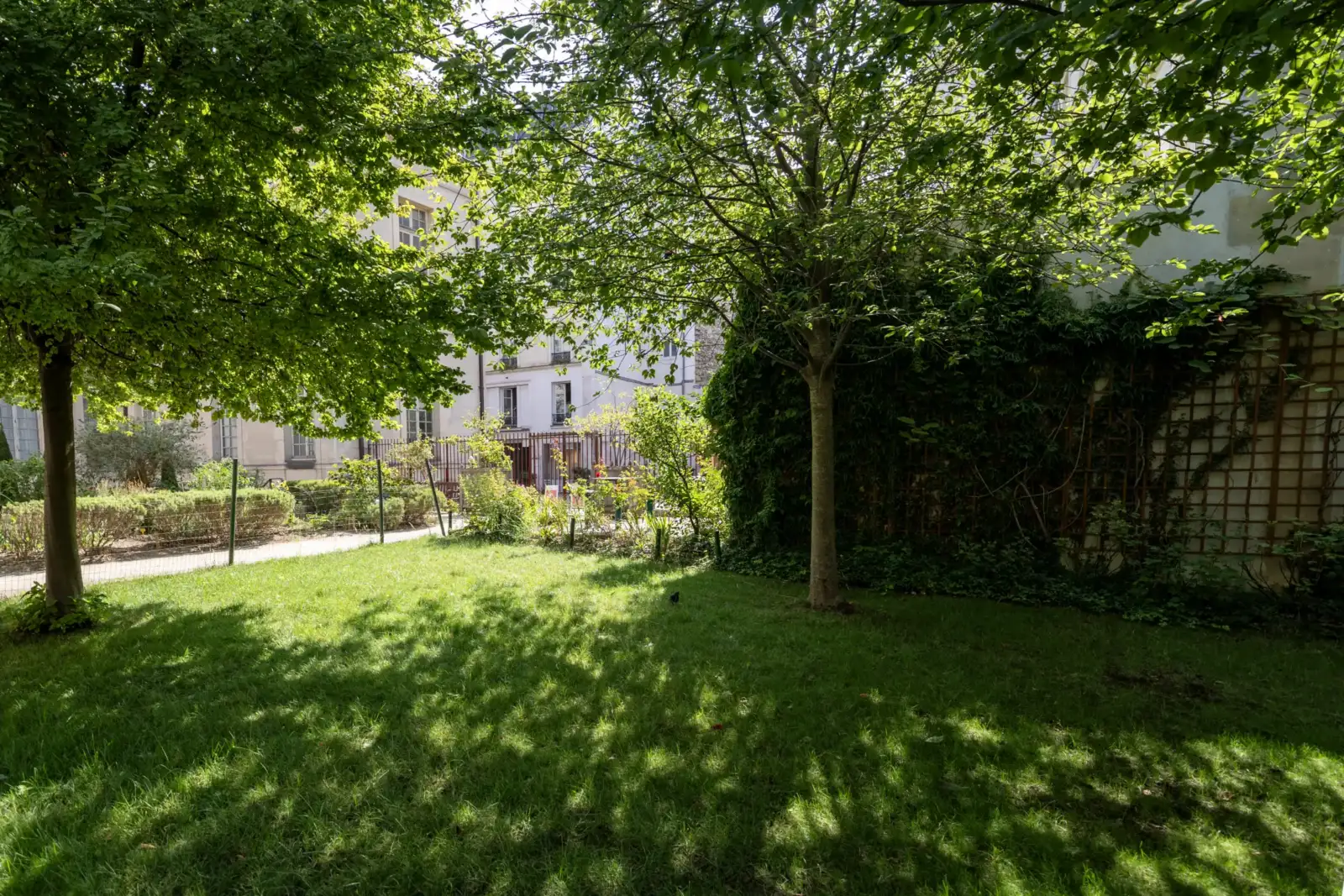 Une pelouse verdoyante et ombragée entourée d'arbres feuillus dans un jardin parisien paisible.