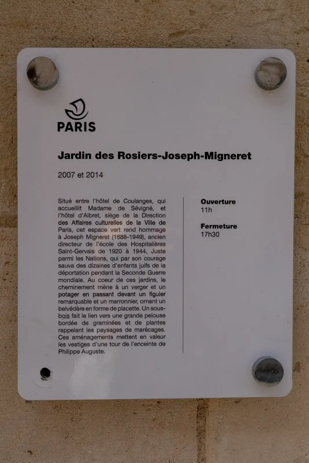 Panneau blanc d'information du jardin des Rosiers Joseph Migneret fixé sur un mur.