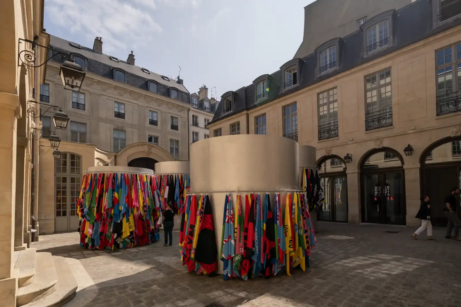 Une cour pavée de Paris abrite des colonnes décorées de foulards colorés.