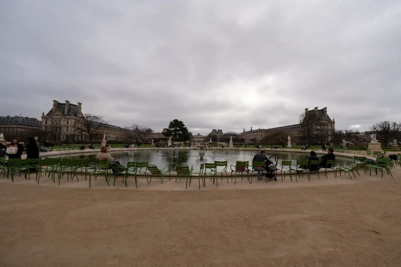Des gens sont assis sur des chaises vertes autour du bassin des Tuileries parisiennes.