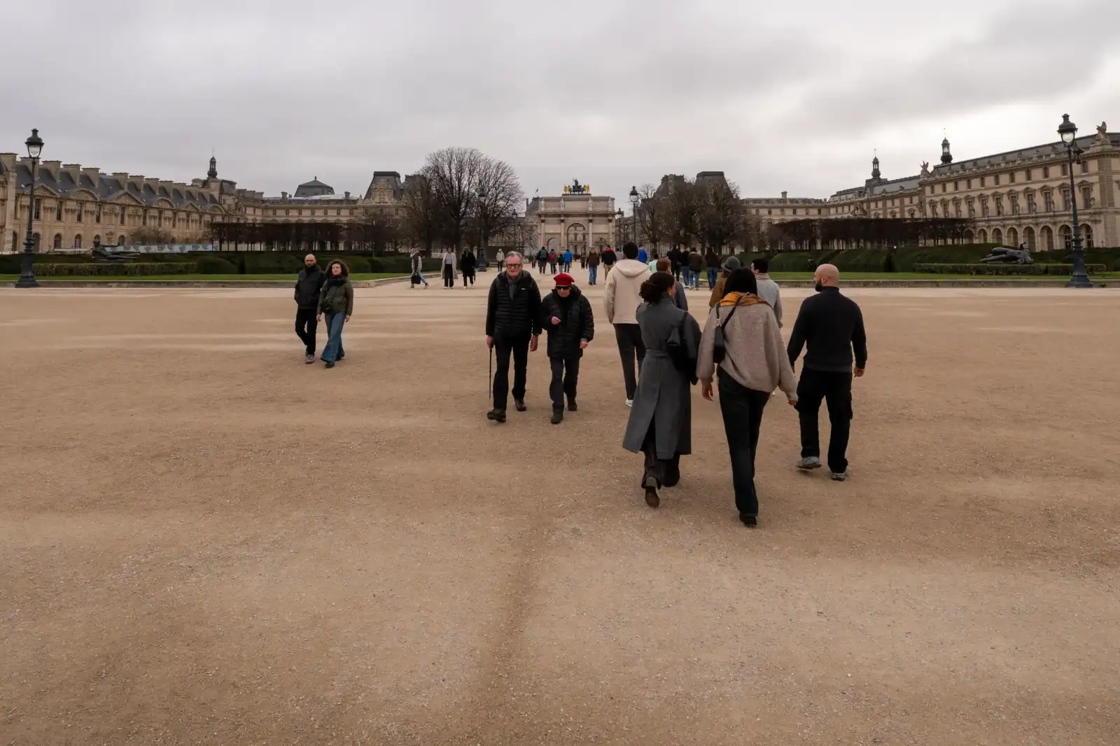Des gens marchent sur le sol sablonneux devant la façade du jardin des Tuileries.