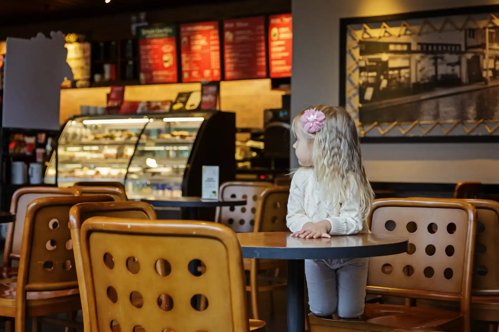 Une petite fille blonde avec une fleur rose est assise à une table dans un café.