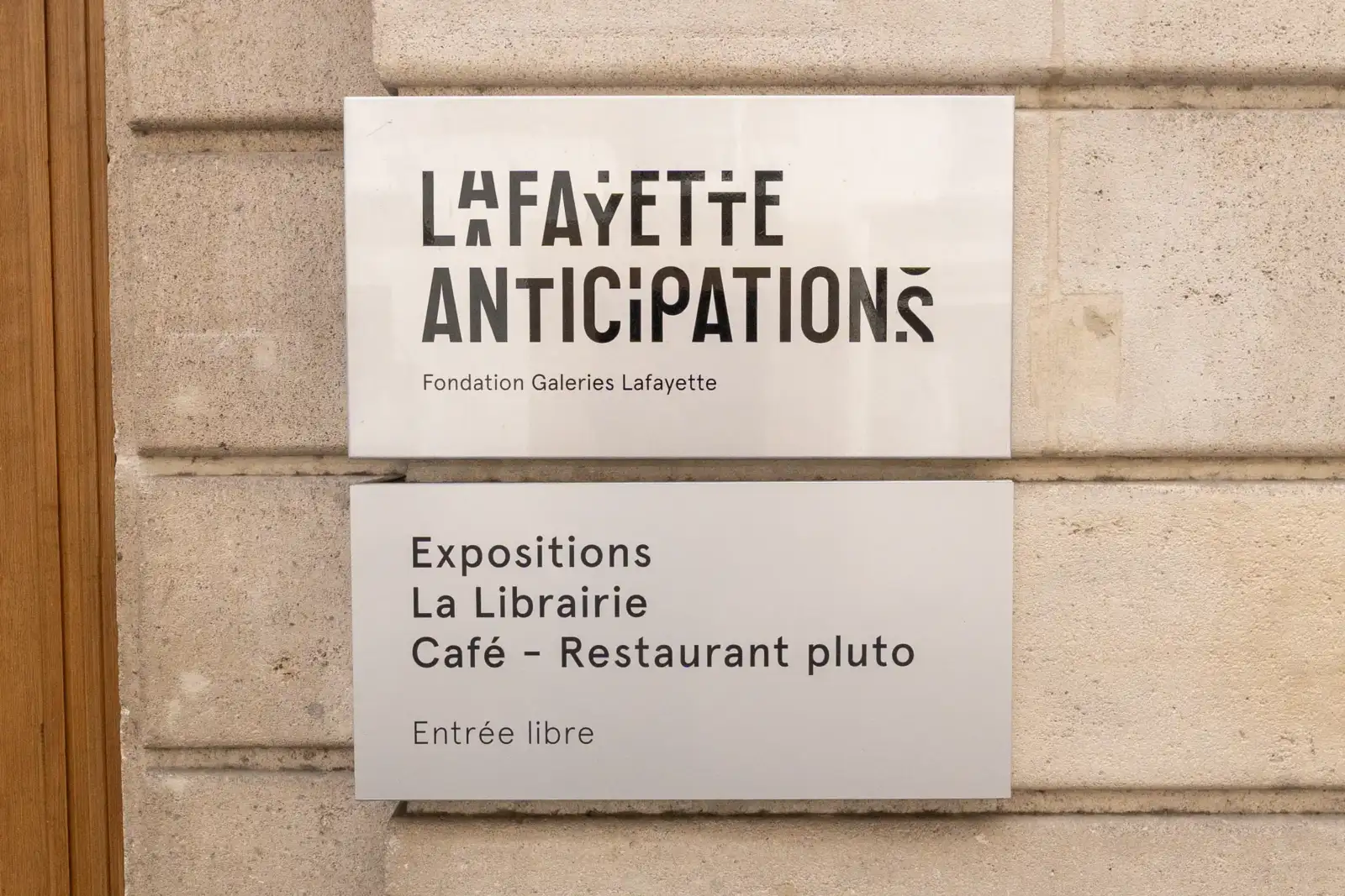 Panneaux indicateurs en métal blanc fixés sur un mur de pierres claires.