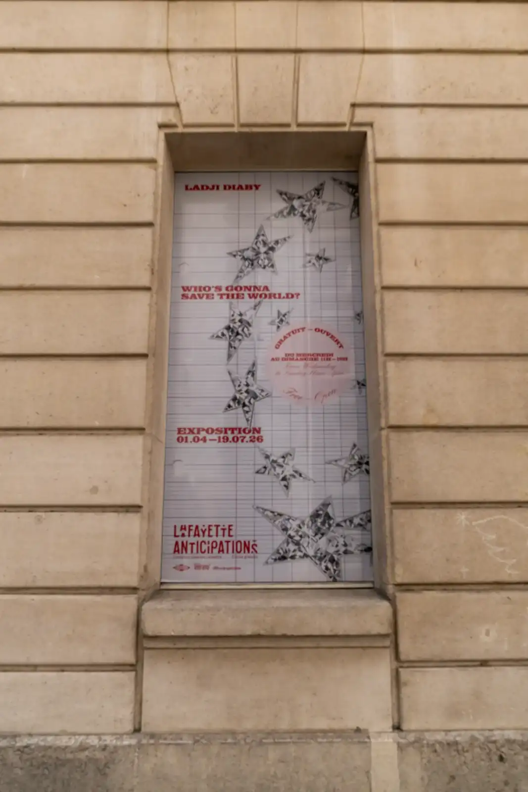 Une affiche d'exposition pour Lafayette Anticipations est encastrée dans un mur en pierre beige.