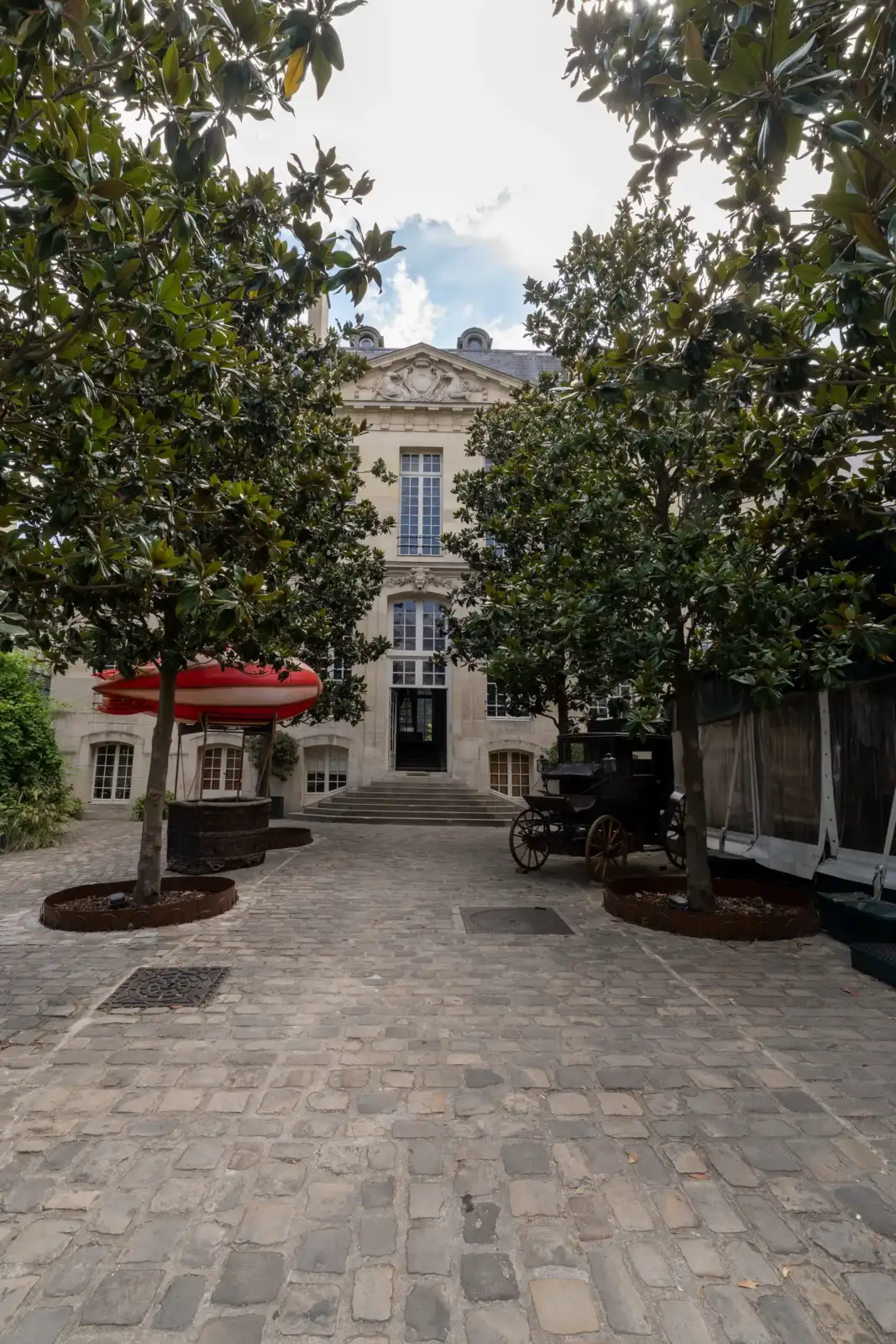 La façade classique d’un hôtel parisien s'ouvre sur une cour pavée ombragée.