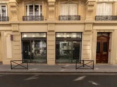 Façade en pierre beige d une librairie parisienne avec des grilles métalliques fermées.
