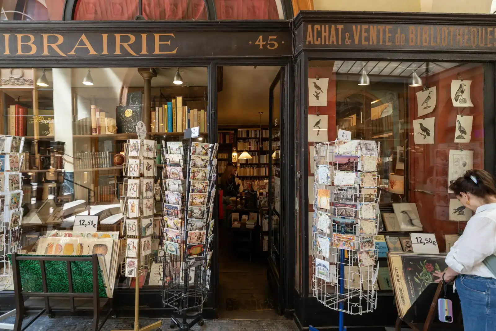 Une femme regarde des cartes postales devant la librairie Jousseaume à Paris.