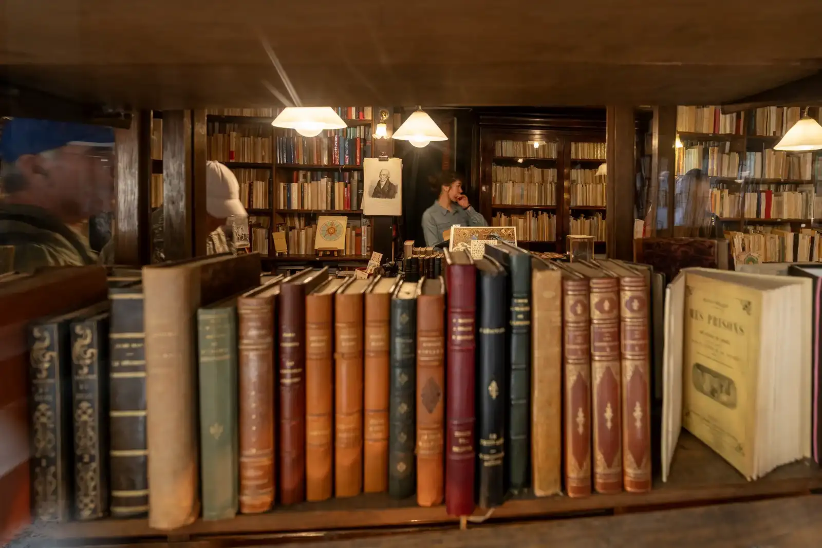 Une librairie ancienne parisienne montre des étagères remplies de livres et une vendeuse.