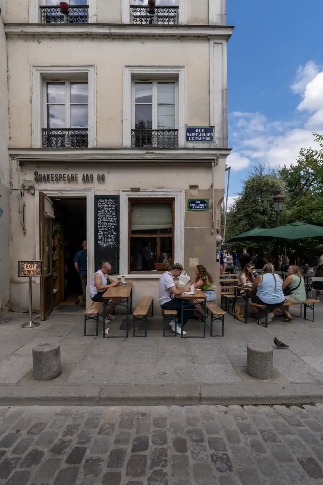 Vue de face de la librairie Shakespeare and Company à Paris avec des clients attablés.