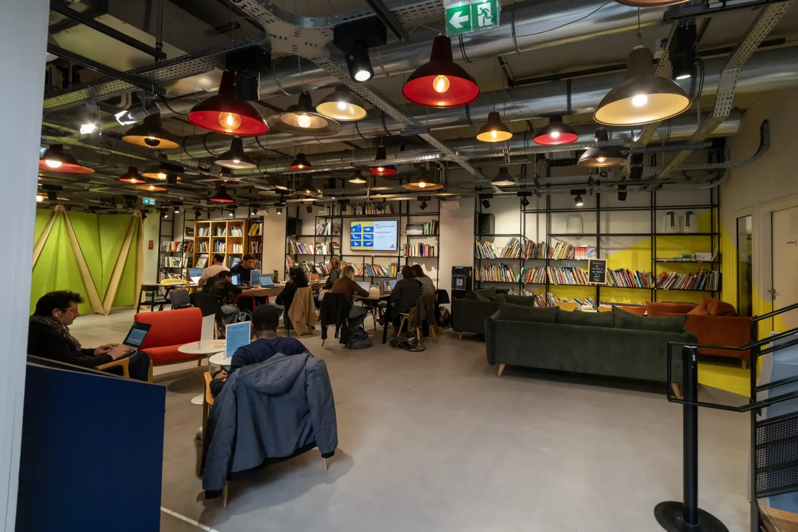 Espace de coworking moderne au MAIF Social Club avec des étagères remplies de livres.