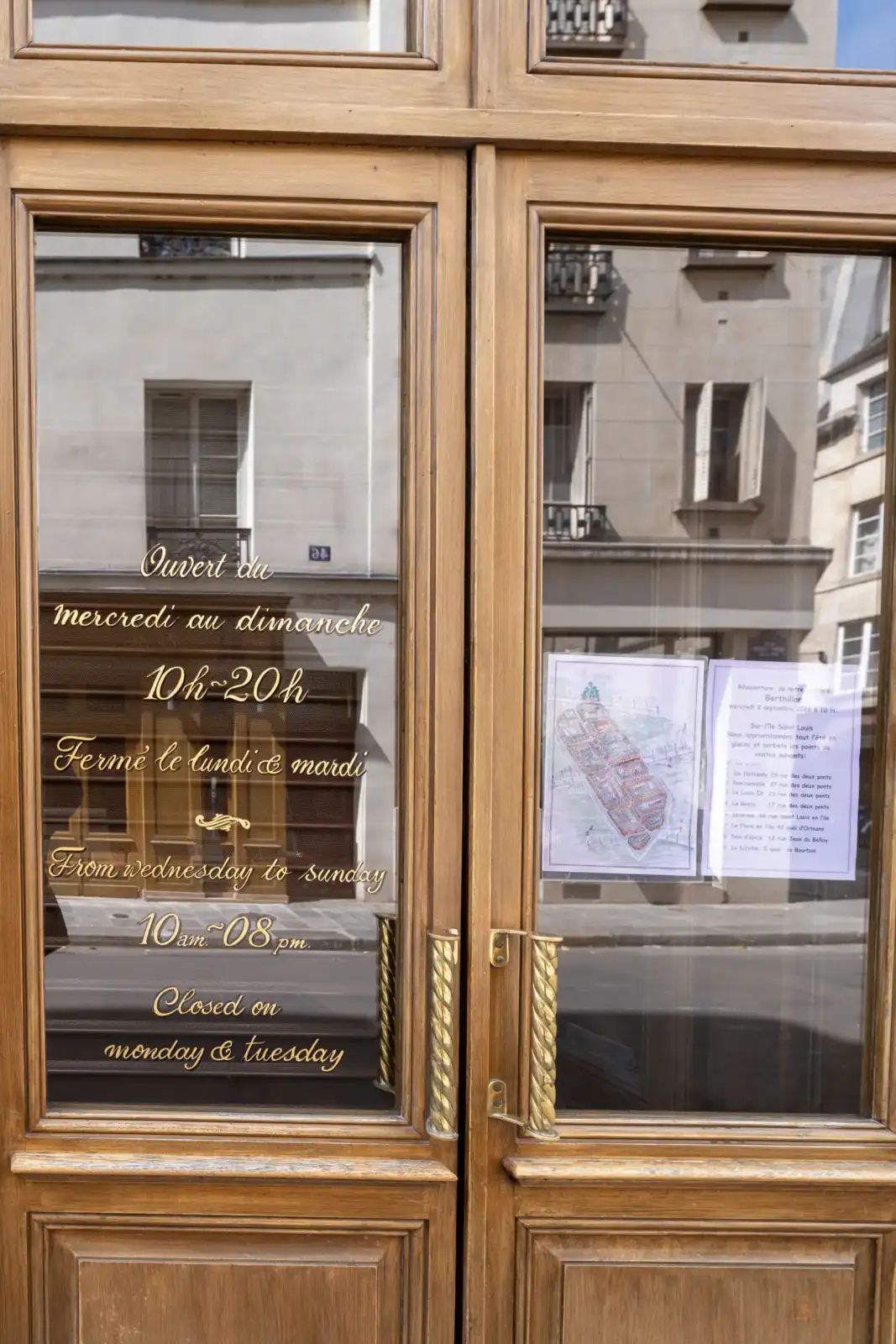 Porte en bois vitrée avec des inscriptions dorées indiquant les horaires d ouverture.