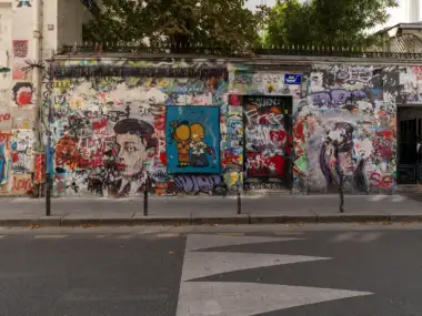 Une rue parisienne présente un mur de bâtiment couvert de graffitis multicolores et de peintures.