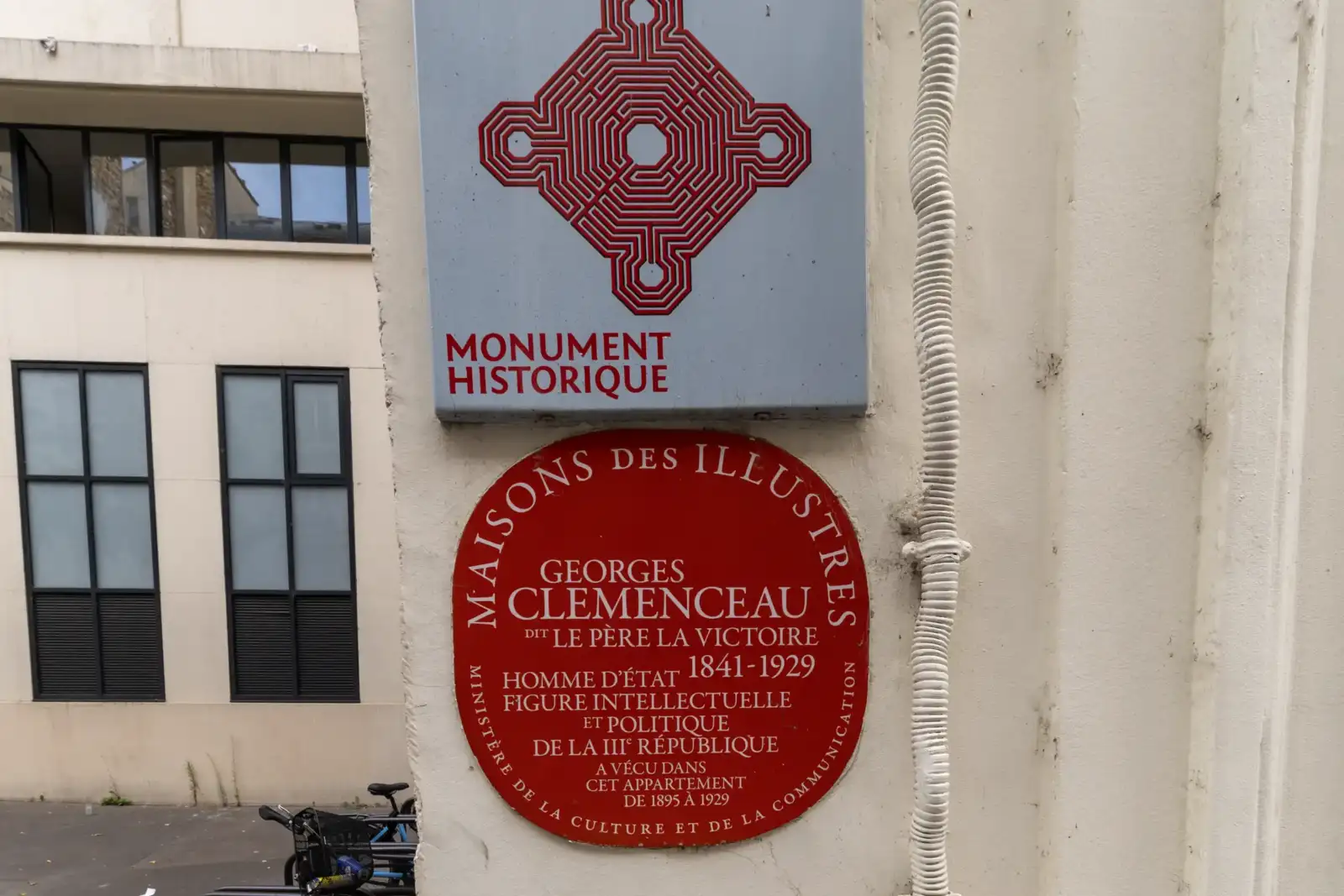 Gros plan sur deux plaques signalétiques accrochées à un mur extérieur blanc.