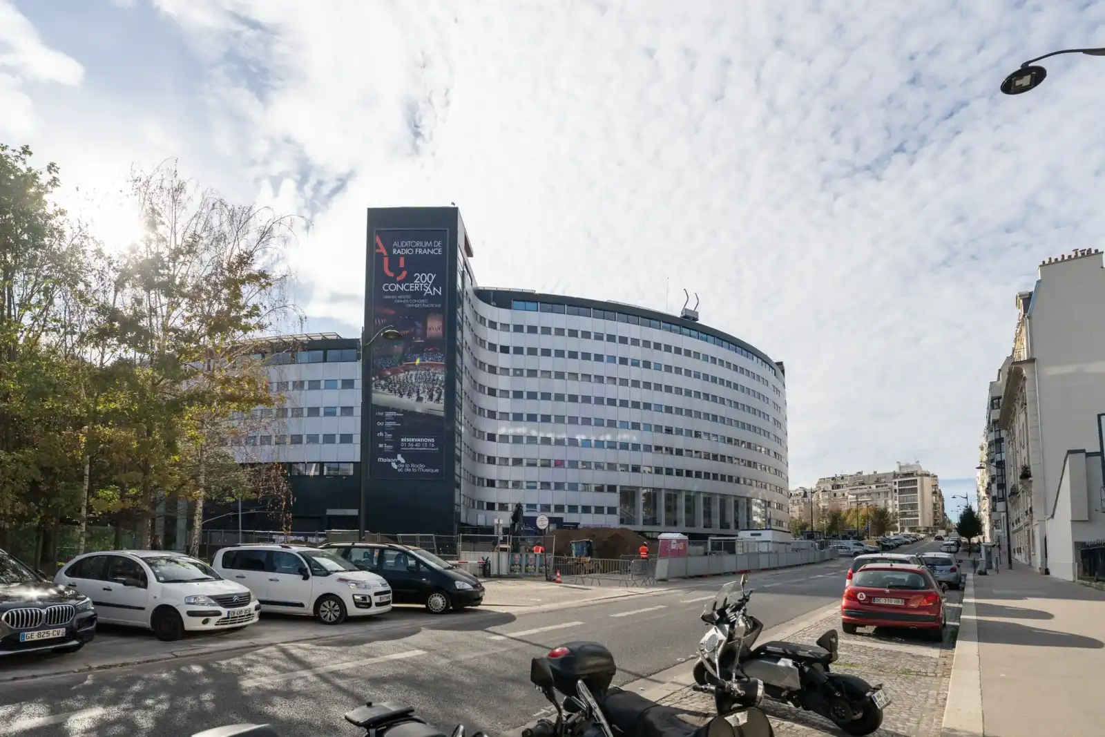 Vue extérieure de la Maison de la Radio à Paris avec des voitures garées devant.