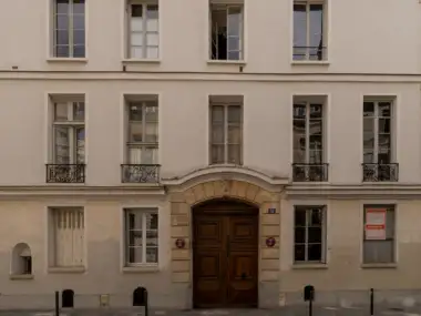 Façade claire avec une grande porte en bois et des fenêtres alignées symétriquement.