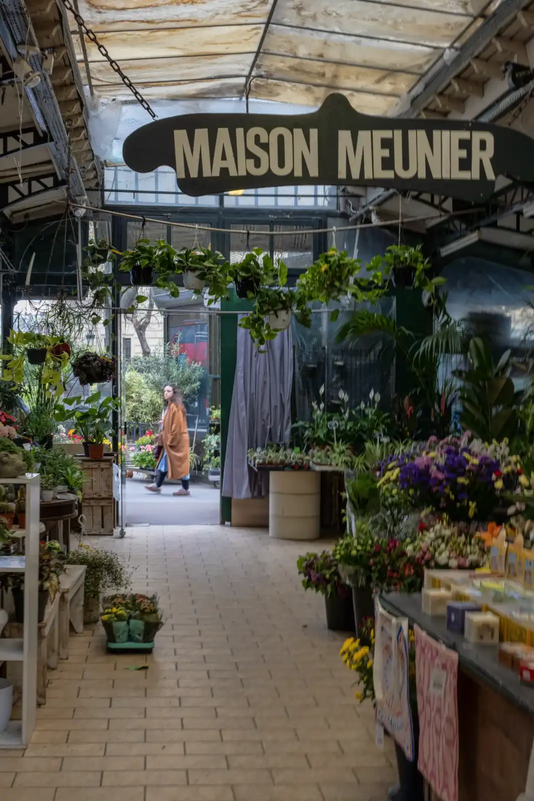 Une femme marche devant le fleuriste Maison Meunier au marché aux fleurs parisien.