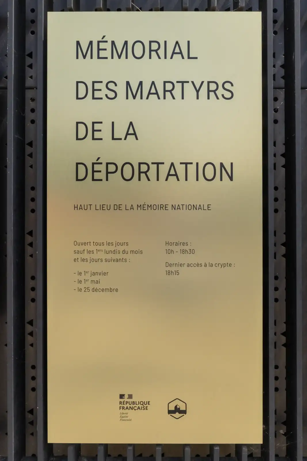 Une plaque commémorative dorée indique les horaires et informations du Mémorial des Martyrs de la Déportation.