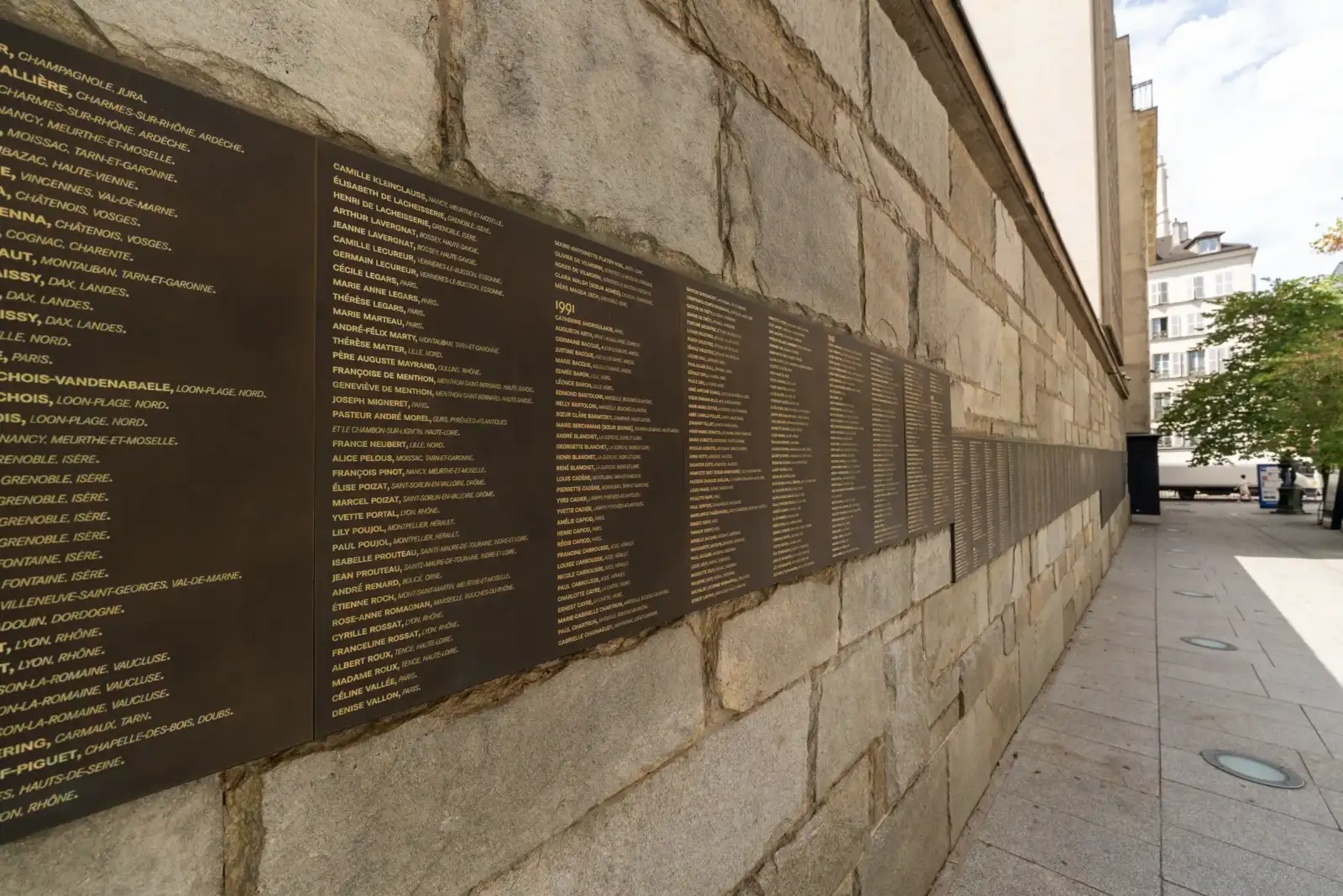 Des plaques de bronze gravées de noms de victimes sont fixées sur un mur en pierre.