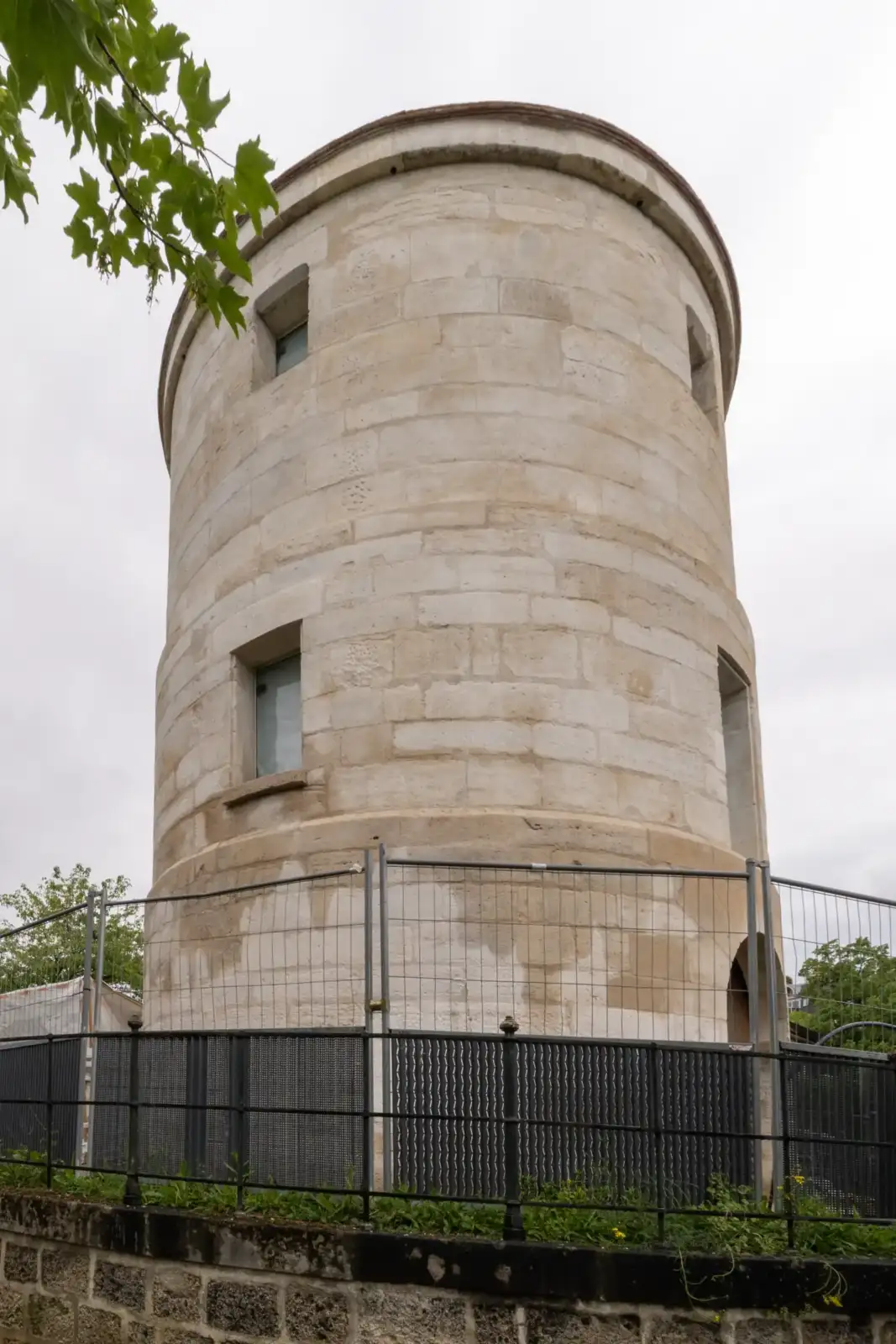 Vue en contre-plongée de l'ancienne tour en pierre de Charité entourée d'une clôture.