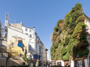 Une rue parisienne présente un mur végétal luxuriant face à une fresque murale colorée.