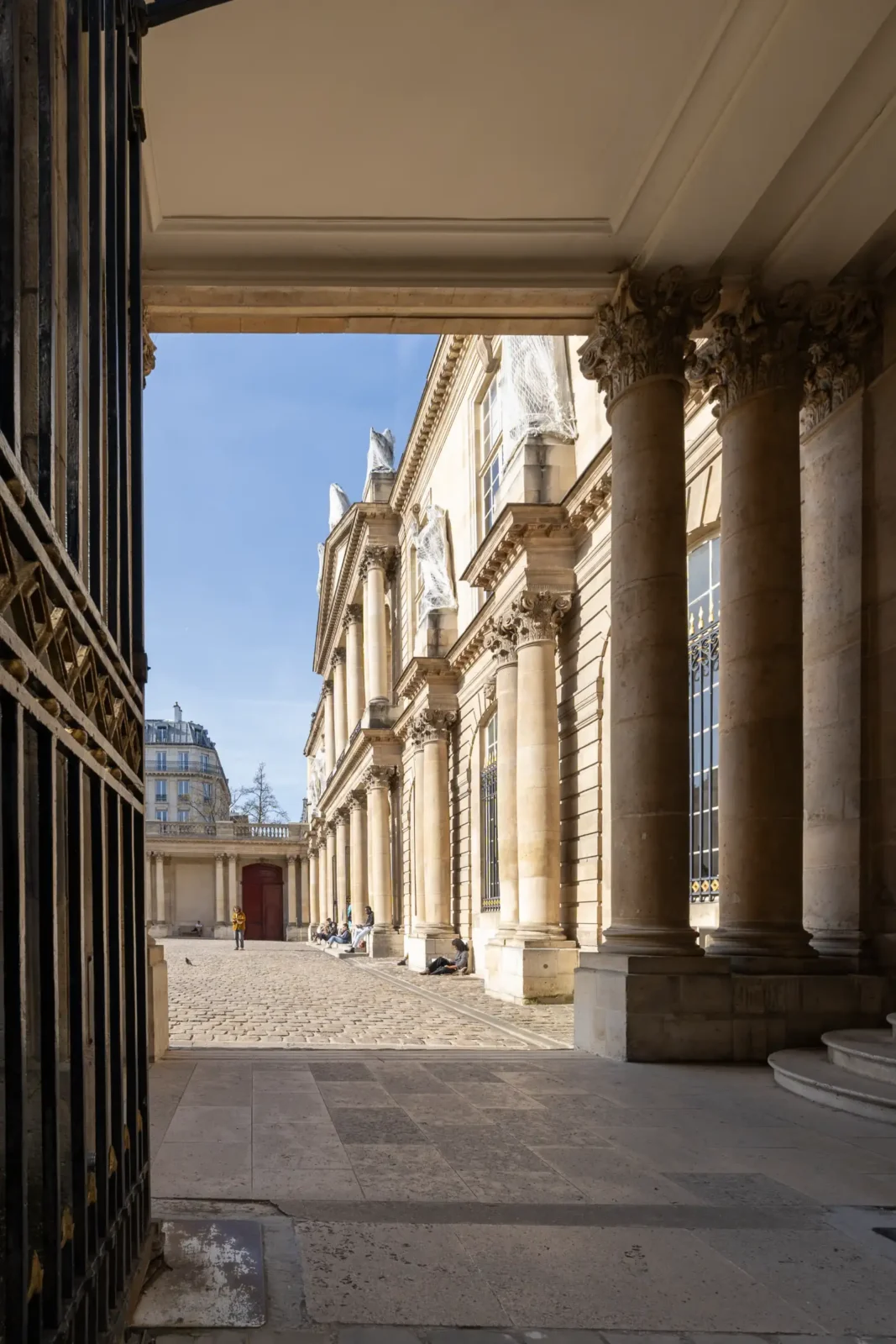 La cour pavée du musée des Archives nationales vue à travers une porte monumentale.