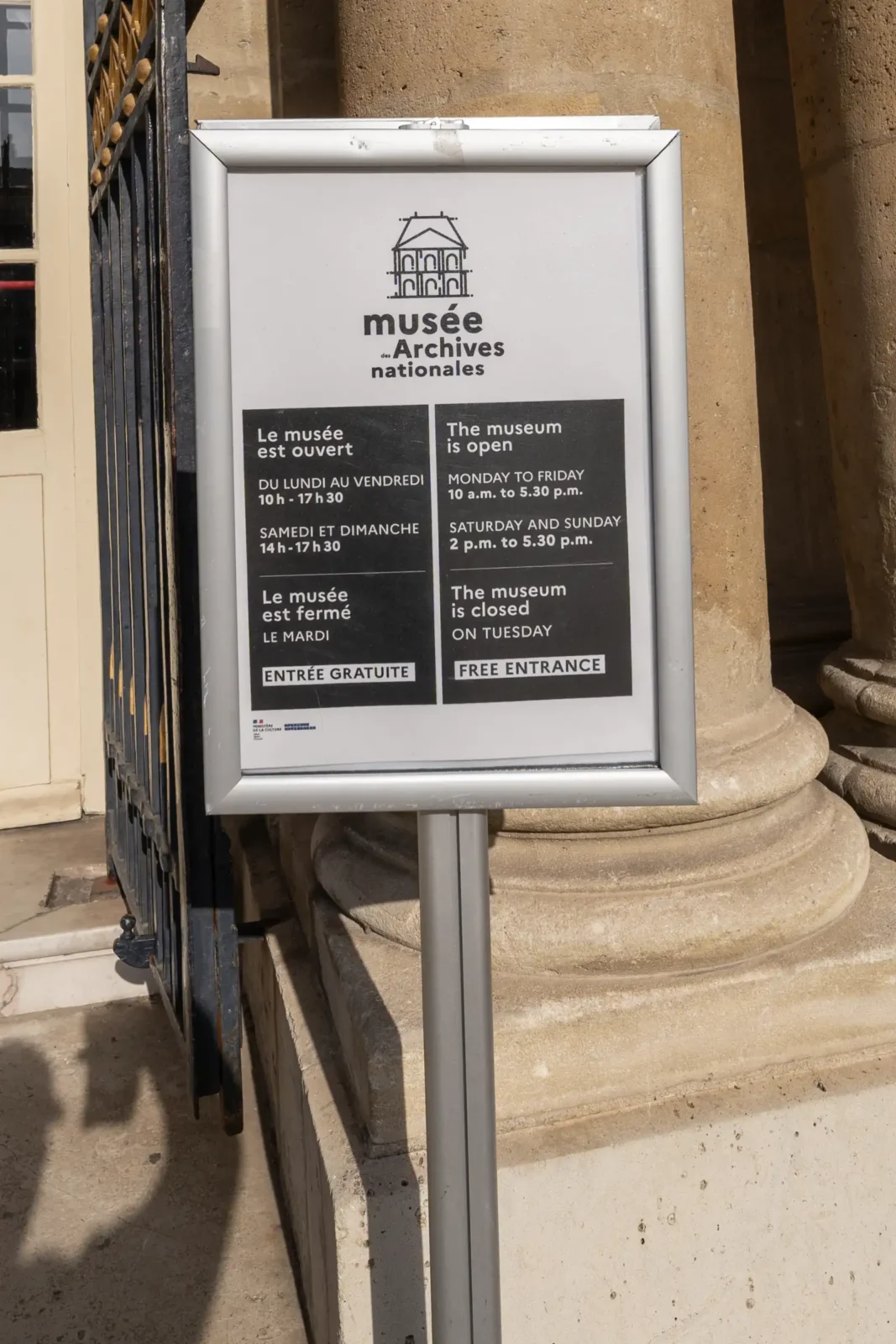 Panneau d'information bilingue affichant les horaires du Musée des Archives nationales à Paris.