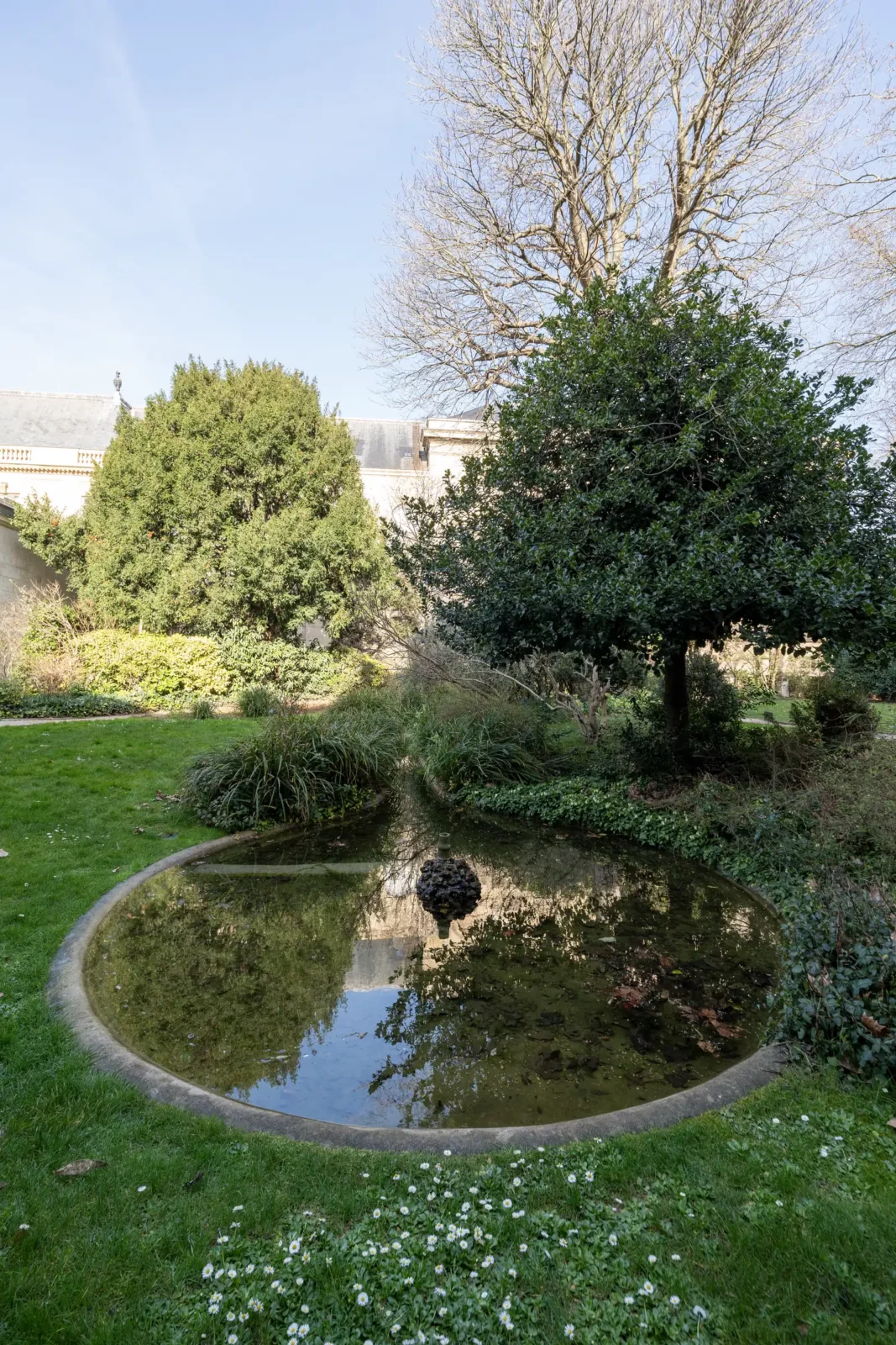 Un bassin circulaire entouré de verdure dans le jardin des Archives nationales à Paris.