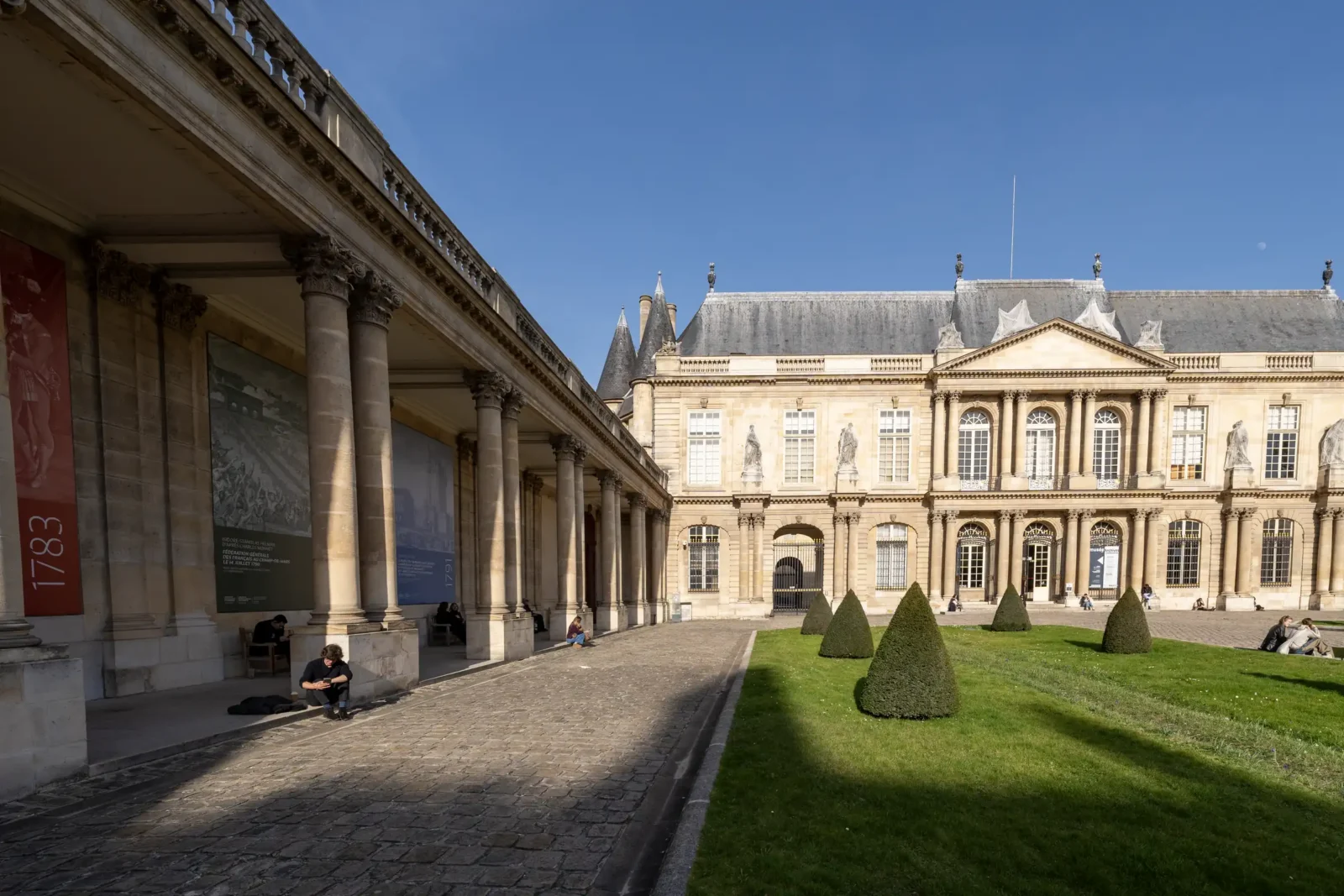 La cour pavée et le jardin du musée des Archives nationales sous un ciel bleu.