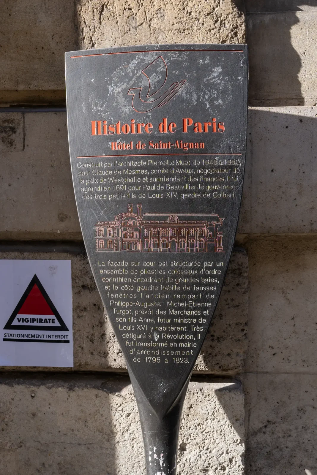 Une plaque historique en forme de bouclier fixée sur un mur en pierre calcaire.