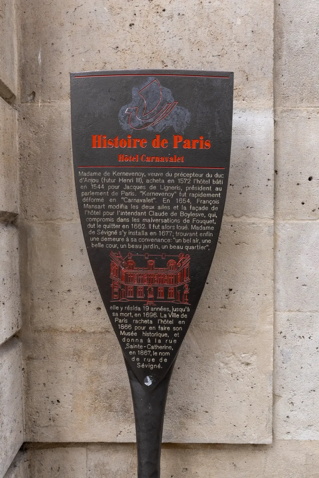 Panneau informatif noir sur l'histoire de l'hôtel Carnavalet fixé sur un mur pierre.