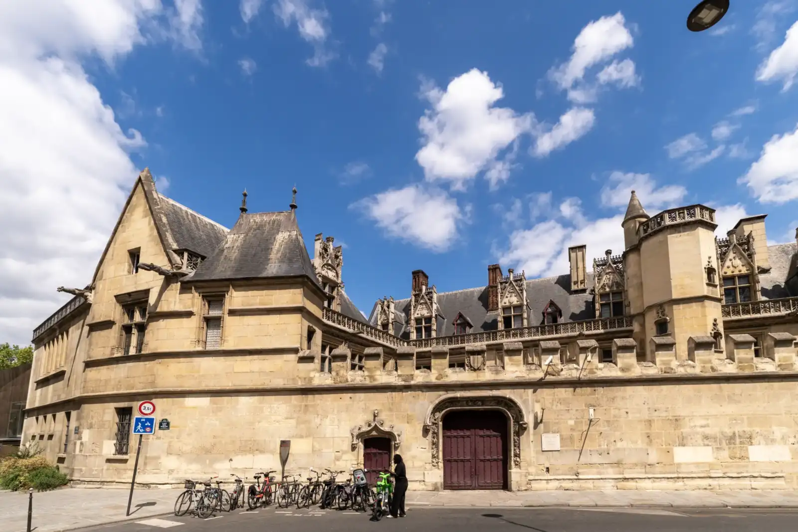 La façade médiévale en pierre du musée de Cluny sous un ciel bleu nuageux.