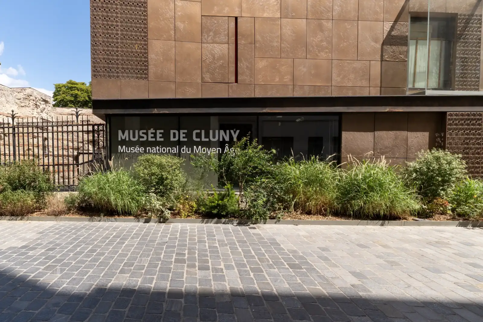 Entrée moderne du Musée de Cluny avec sa signalétique en lettres blanches sur vitre.