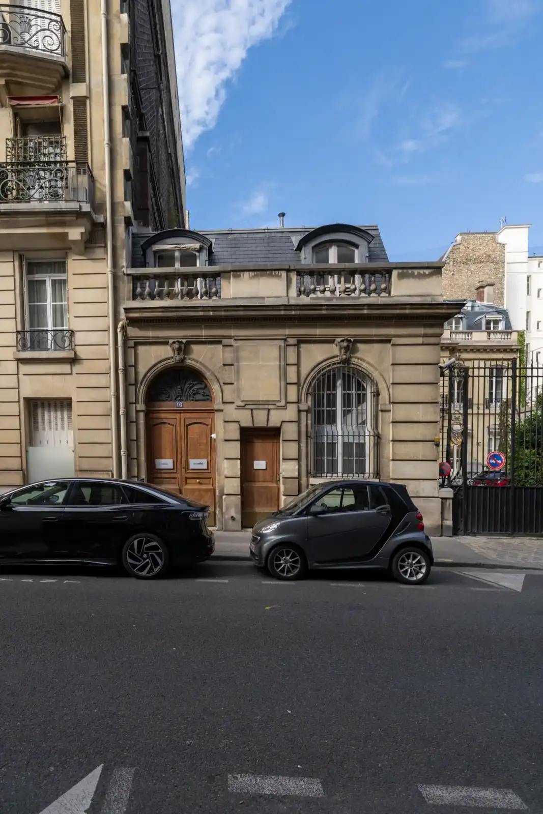 Une façade parisienne classique en pierre avec deux voitures garées sous un ciel bleu.