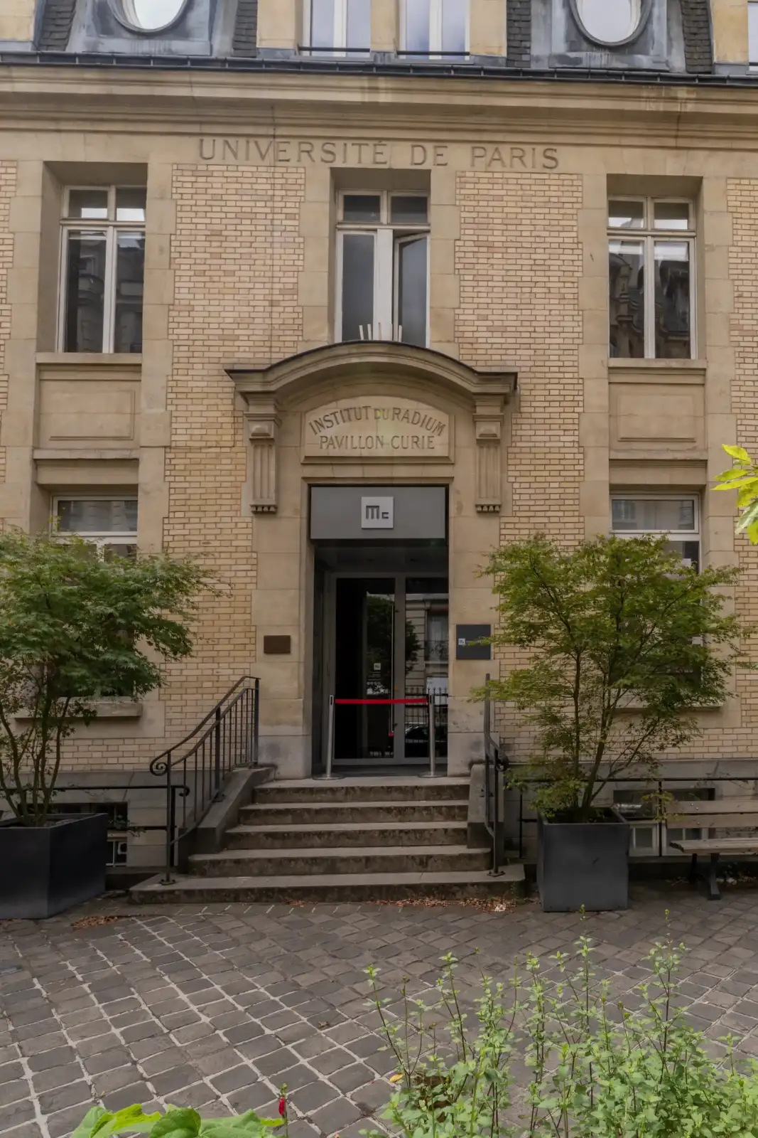 La façade en briques beiges du Pavillon Curie avec ses fenêtres et son entrée principale.