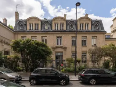 La façade classique du Musée Curie à Paris avec trois voitures garées devant.