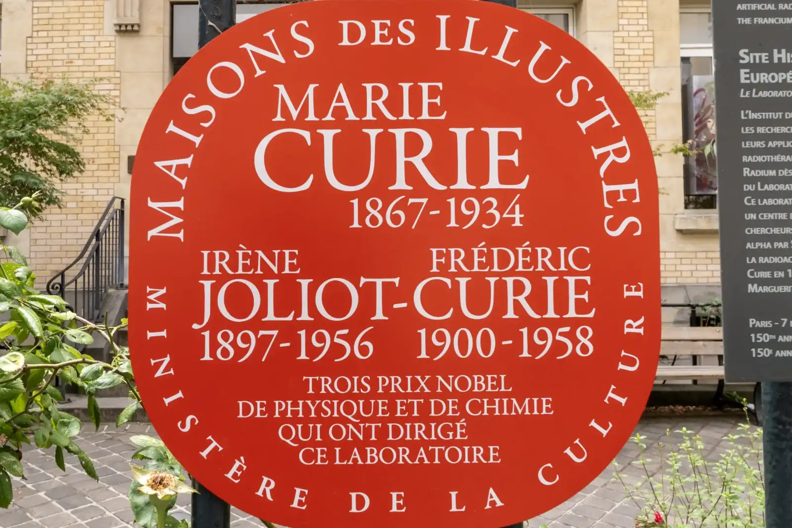Un panneau rouge ovale indique la maison des illustres Marie et Irène Joliot-Curie.
