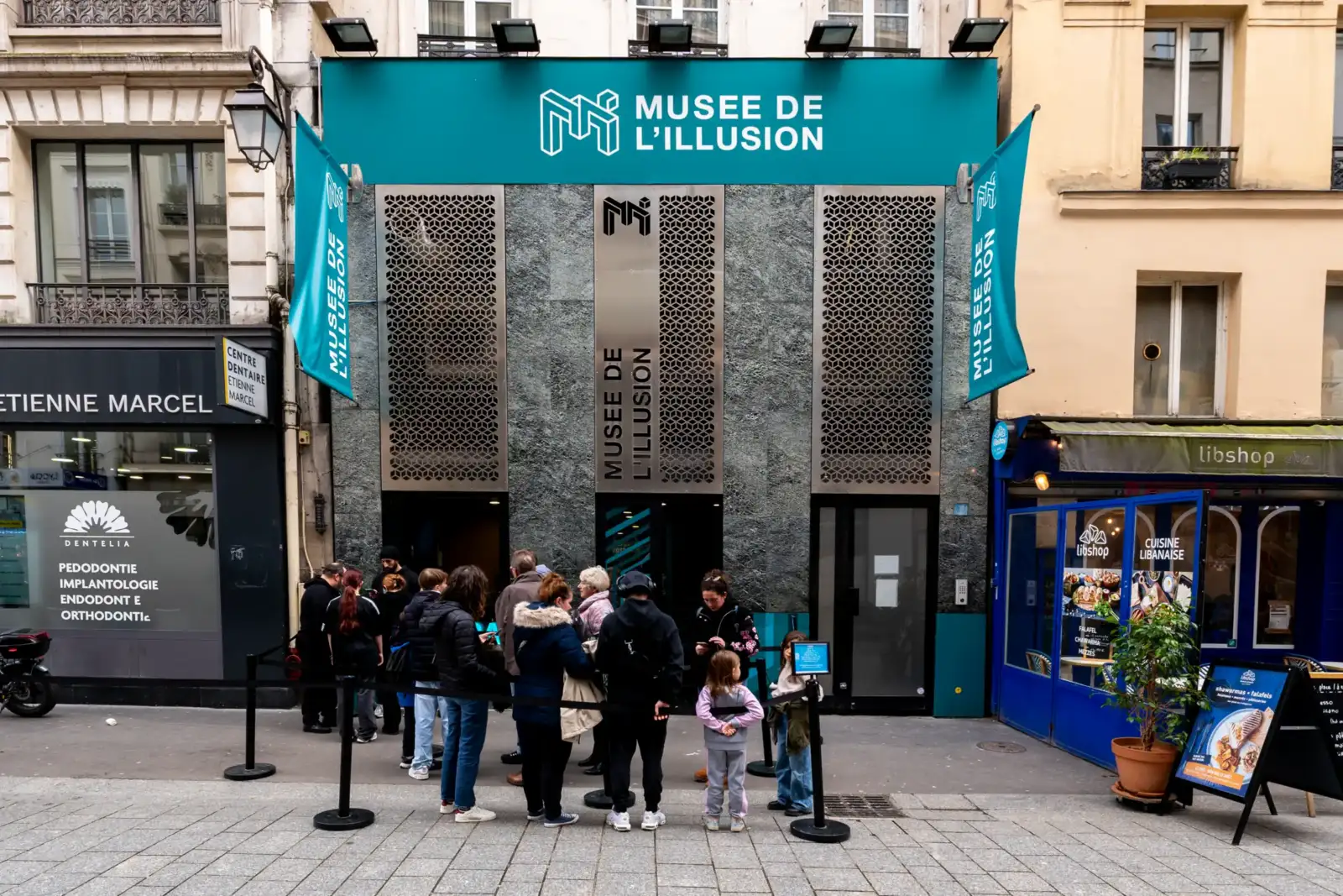 Des visiteurs font la queue devant la façade moderne du Musée de l'Illusion parisien.