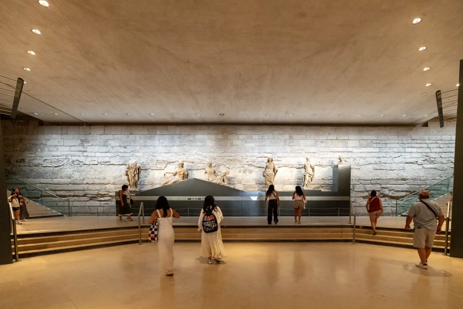Des visiteurs admirent des statues anciennes exposées devant un grand mur en pierre.