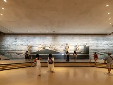 Des visiteurs admirent des statues anciennes exposées devant un grand mur en pierre.