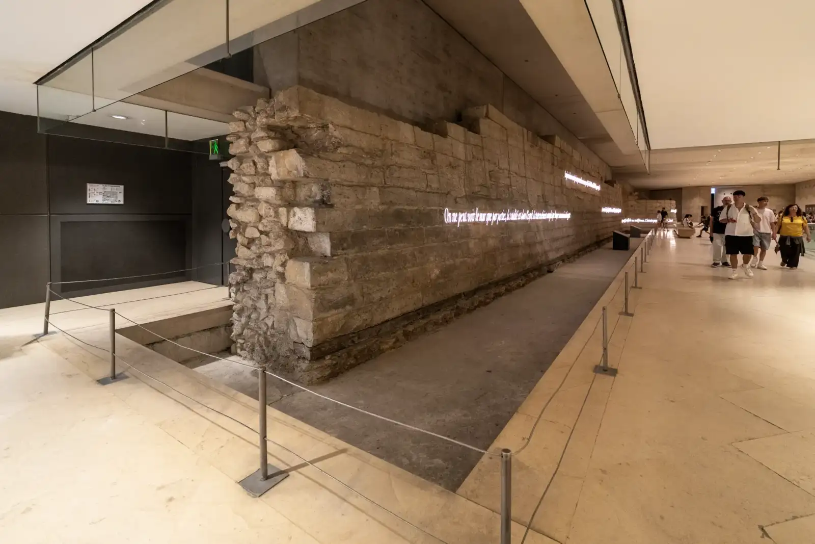 Un mur médiéval en pierre avec des inscriptions lumineuses dans le musée du Louvre.