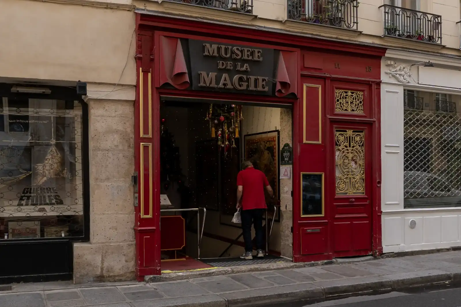 Un homme entre dans le Musée de la Magie à la devanture rouge parisienne.
