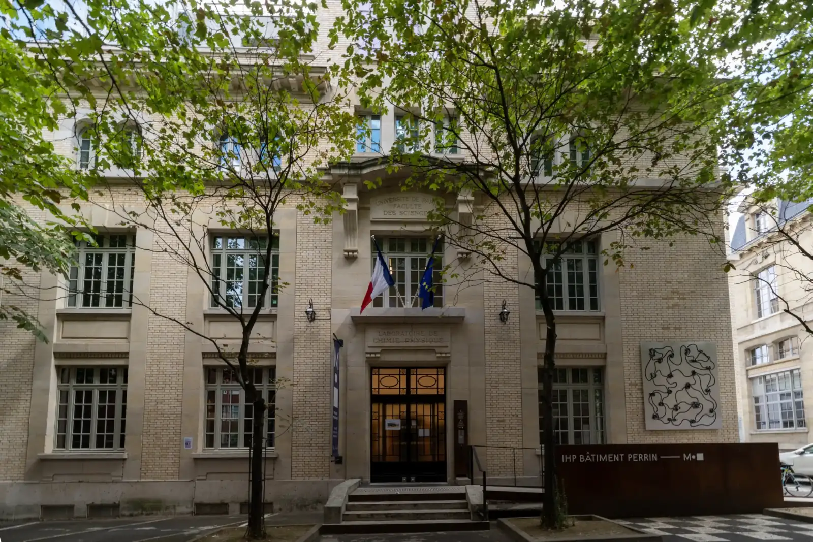Facade claire de la Maison Poincare encadree par deux arbres feuillus a Paris.