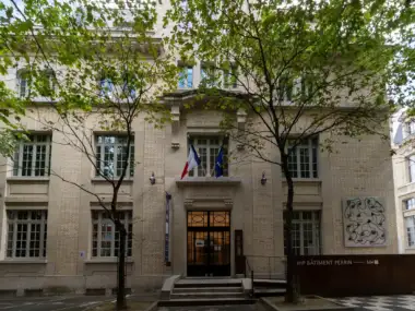 Facade claire de la Maison Poincare encadree par deux arbres feuillus a Paris.