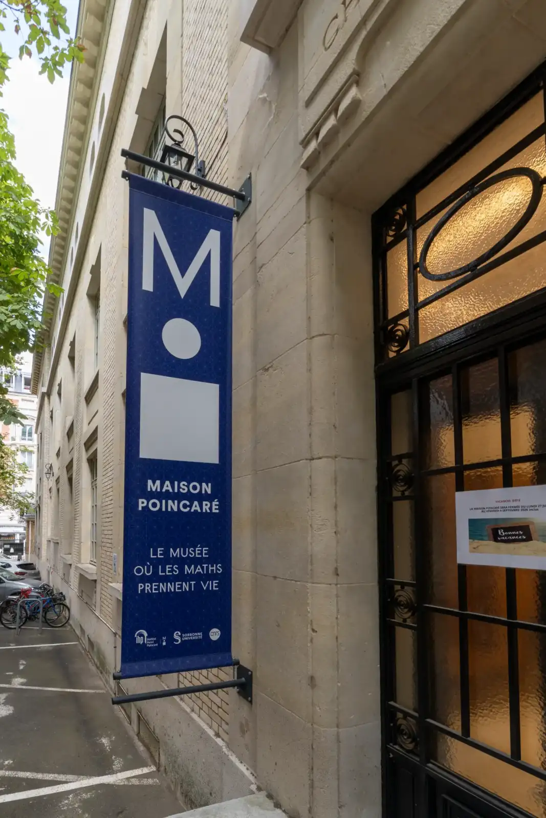 Une longue bannière bleue de la Maison Poincaré est accrochée sur un mur extérieur.