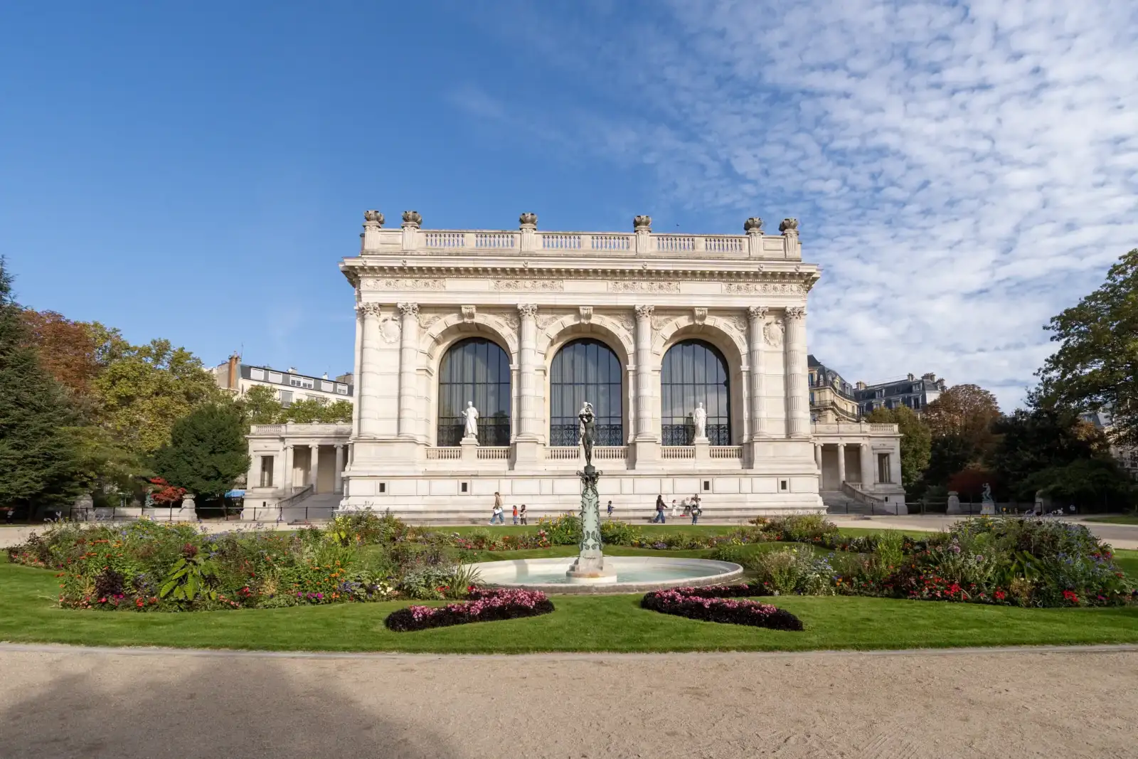 Façade ensoleillée du Palais Galliera à Paris avec une fontaine et des parterres fleuris.