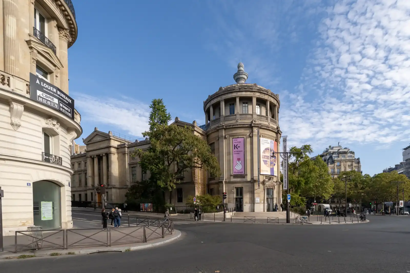 La façade monumentale du Musée National des Arts Asiatiques Guimet s'élève sous un ciel bleu nuageux.