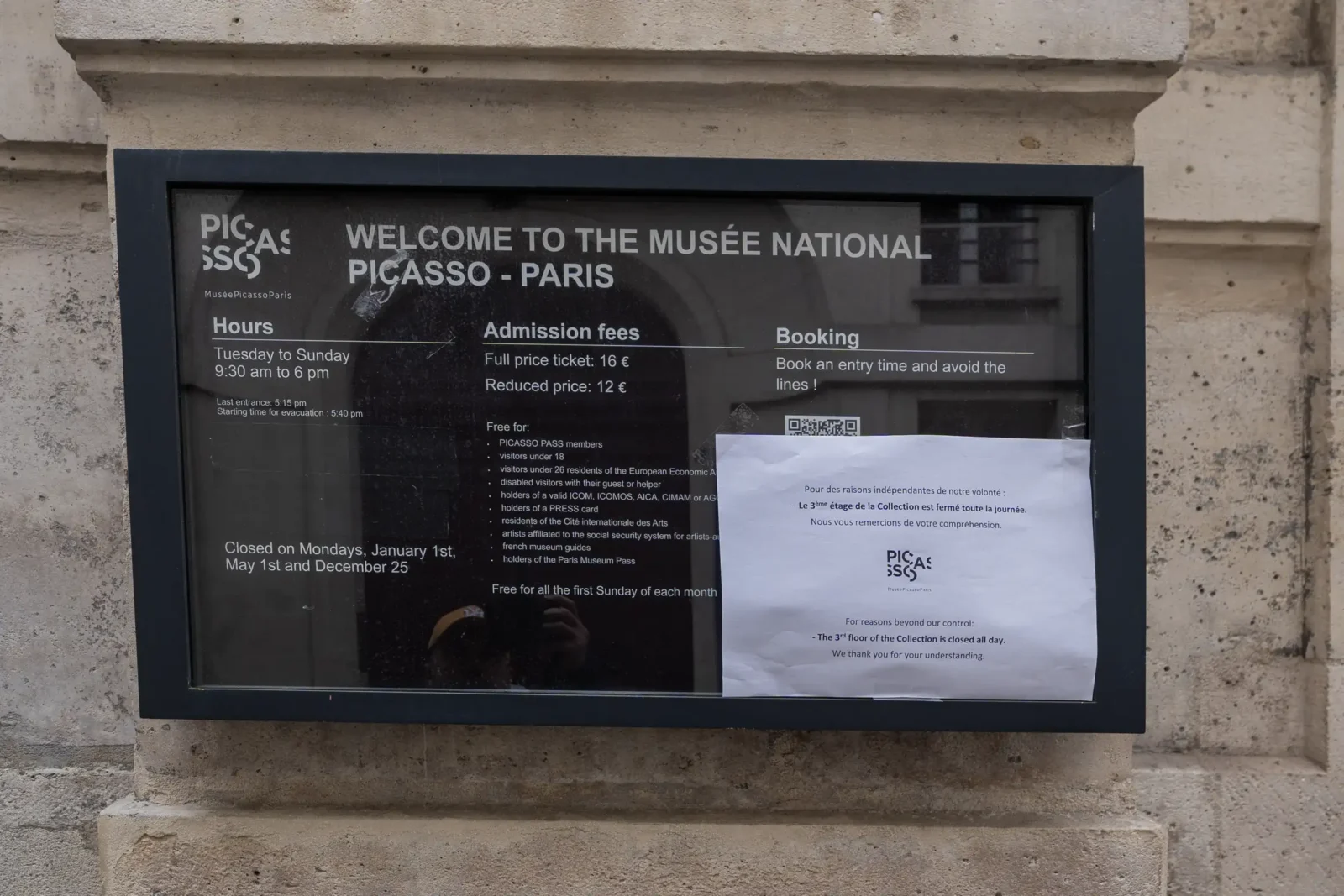 Panneau d'information noir sur un mur en pierre affichant les tarifs du Musée Picasso.