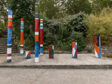 Plusieurs colonnes cylindriques peintes de couleurs vives se dressent sur une estrade en béton au milieu d'un parc parisien.